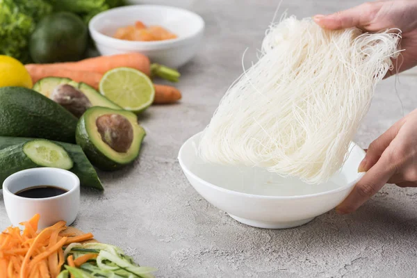 Cropped view of woman putting noddles to white bowl with water — Stock Photo