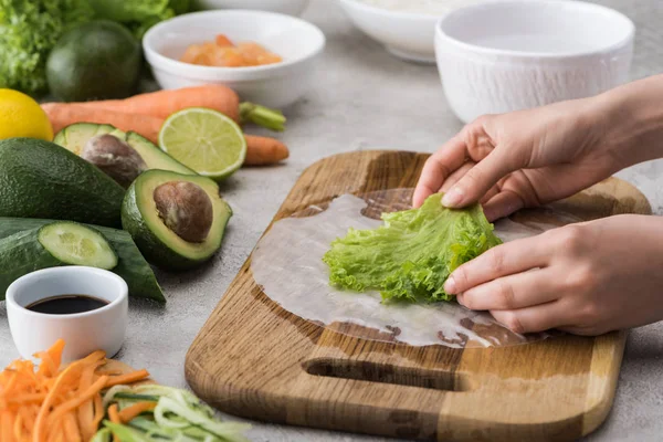 Vista recortada de la mujer poniendo lechuga en el papel de arroz, en la tabla de cortar - foto de stock