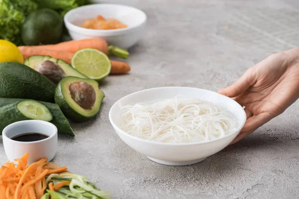 Cropped view of woman holding white bowl with noddles and water — Stock Photo