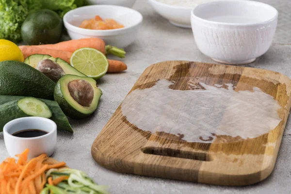 Rice paper with water on cutting board among ingredients — Stock Photo