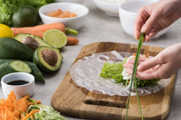 Vista recortada de la mujer poniendo cebolla en el pepino cortado, zanahoria, lechuga y papel de arroz - foto de stock