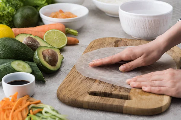 Vista recortada de la mujer poniendo papel de arroz en la tabla de cortar entre los ingredientes - foto de stock