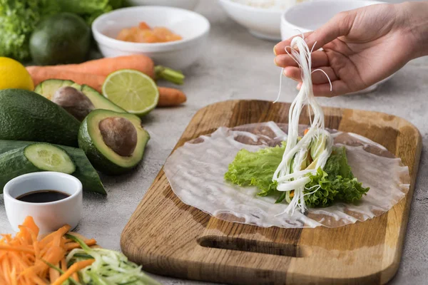 Vista cortada da mulher colocando macarrão em papel de alface e arroz na tábua de corte — Fotografia de Stock