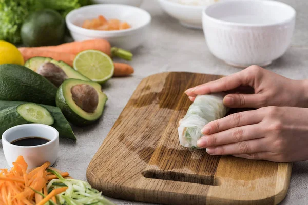 Vista parcial de la mujer haciendo rollo de primavera en la tabla de cortar - foto de stock