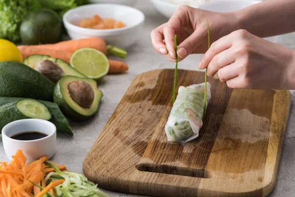 Vista ritagliata della donna legatura rotolo primavera sul tagliere con cipolla — Foto stock