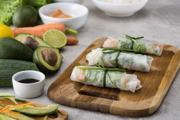 Rouleaux de printemps sur planche à découper avec oignon parmi les ingrédients — Photo de stock