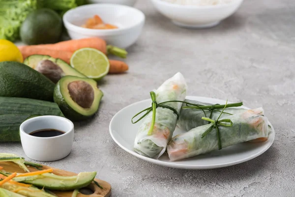 Sabrosos rollos de primavera en plato blanco entre las materias primas - foto de stock