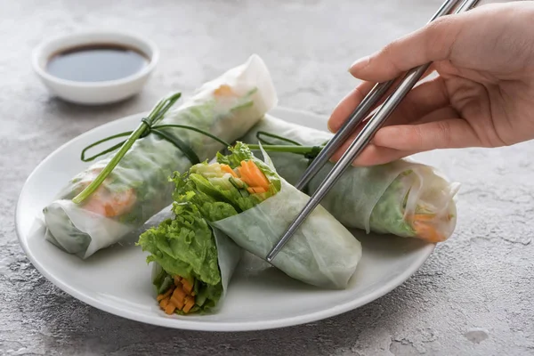 Vue recadrée de femme mangeant des rouleaux de printemps savoureux avec des bâtons en métal — Photo de stock