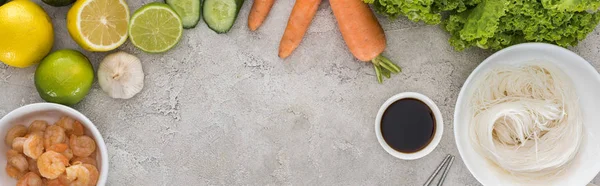 Панорамный снимок лимонов, лаймов, моркови, креветок, соевого соуса, чеснока, лапши и салата на столе — стоковое фото