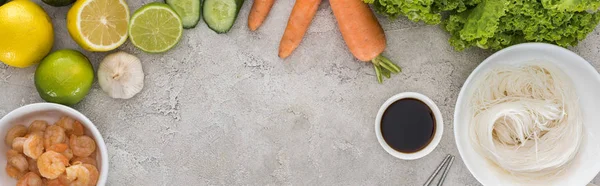 Panoramic shot of lemons, limes, carrots, shrimps, soy sauce, garlic, noodles and lettuce on table — Stock Photo