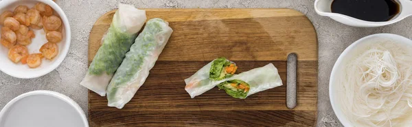 Panoramic shot of spring rolls on cutting board among ingredients — Stock Photo