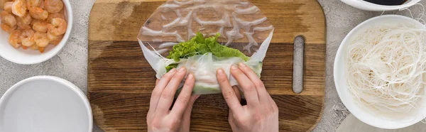 Panoramic shot of woman making roll on cutting board among ingredients — Stock Photo