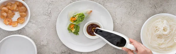 Panoramic shot of woman pouring soy sauce and tasty spring rolls on white plate — Stock Photo