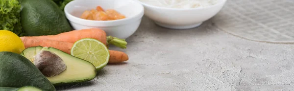 Panoramic shot of lime, avocados, carrots, shrimps, rice paper, noodles on table — Stock Photo