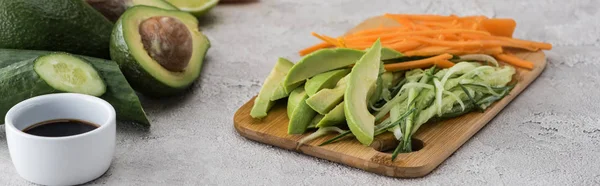 Plano panorámico de aguacate cortado, zanahoria y pepino en la tabla de cortar - foto de stock