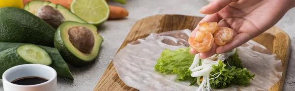 Tiro panorâmico de mulher colocando camarões em alface, macarrão e papel de arroz na tábua de corte — Fotografia de Stock