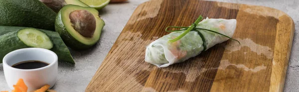 Plano panorámico de rollo de primavera sobre tabla de cortar con cebolla entre ingredientes - foto de stock