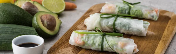 Panoramic shot of spring rolls with soy sauce on cutting board — Stock Photo