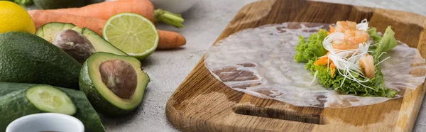 Plano panorámico de lechuga, fideos y camarones sobre papel de arroz, sobre tabla de cortar - foto de stock