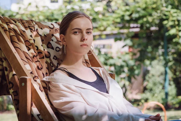 Beautiful blonde girl sitting in deck chair in garden — Stock Photo