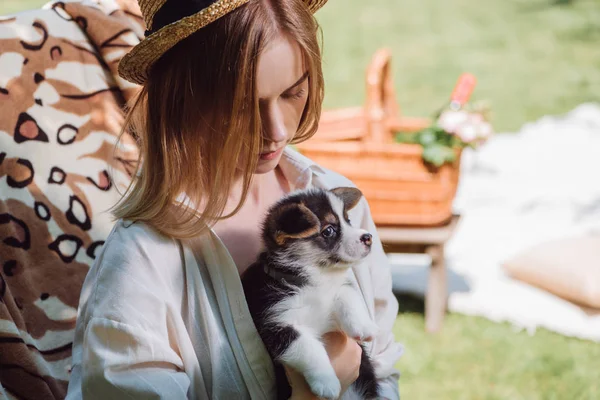 Bionda giovane ragazza in cappello di paglia che tiene il cucciolo mentre è seduto sulla sedia a sdraio in giardino — Foto stock