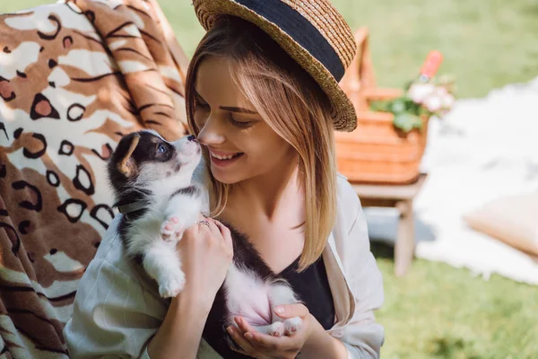 Feliz chica rubia en sombrero de paja mirando cachorro mientras está sentado en la silla de cubierta en el jardín - foto de stock