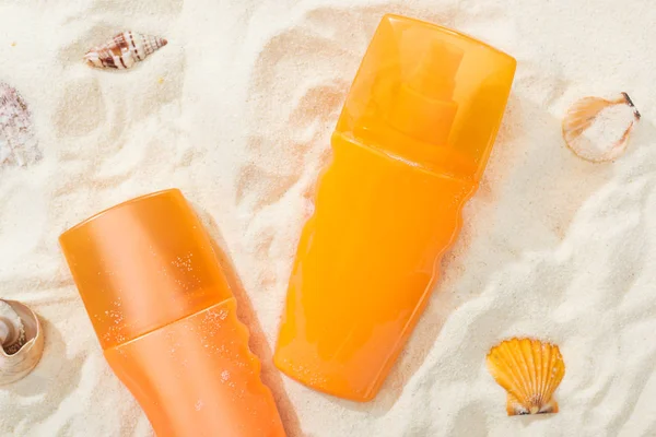 Botellas naranjas de protector solar sobre arena dorada con conchas marinas - foto de stock