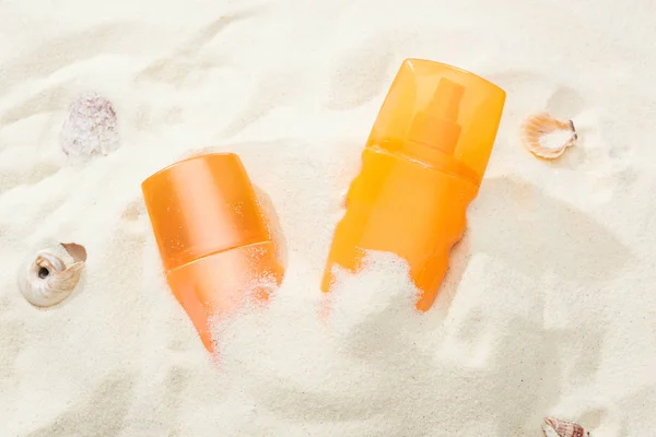 Botellas naranjas de protector solar en arena cerca de conchas marinas - foto de stock