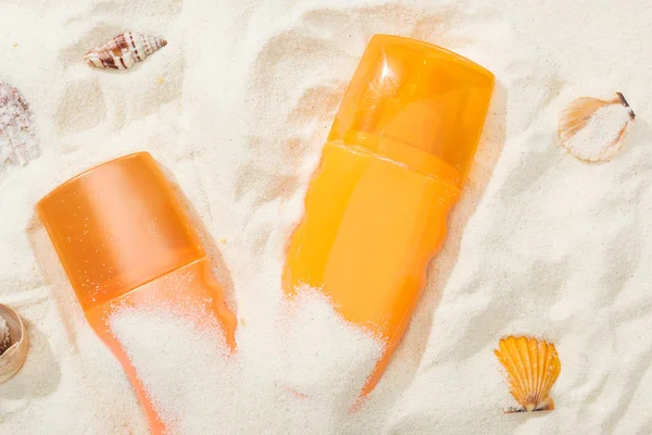 Botellas naranjas de crema solar sobre arena con conchas marinas - foto de stock