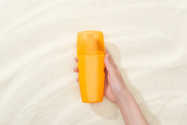 Vista recortada de la mujer sosteniendo protector solar naranja sobre arena dorada - foto de stock