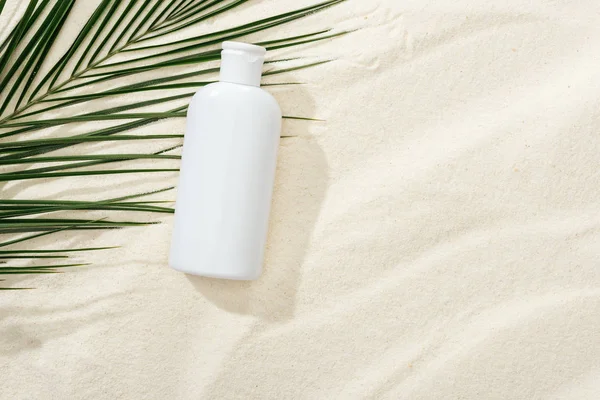 White sunscreen lotion near green palm leaf on sand — Stock Photo