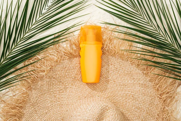Vue de dessus du chapeau de paille élégant sur sable doré avec feuilles de palmier vertes et crème solaire — Photo de stock