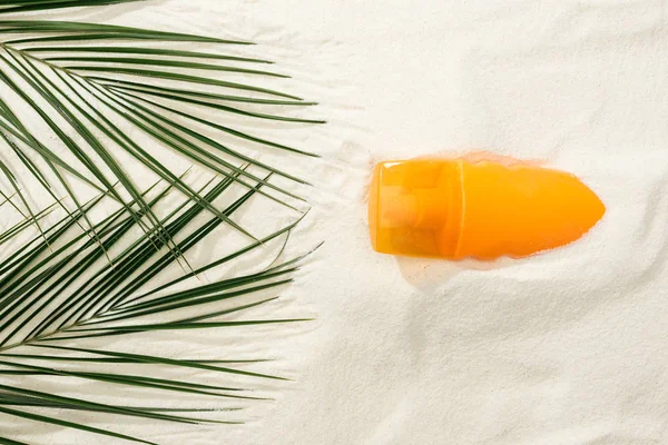 Vue du dessus de la crème solaire et des feuilles de palmier vert sur sable doré — Photo de stock