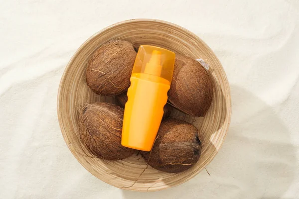 Верхний вид солнцезащитного крема в миске с кокосами на золотом песке — стоковое фото