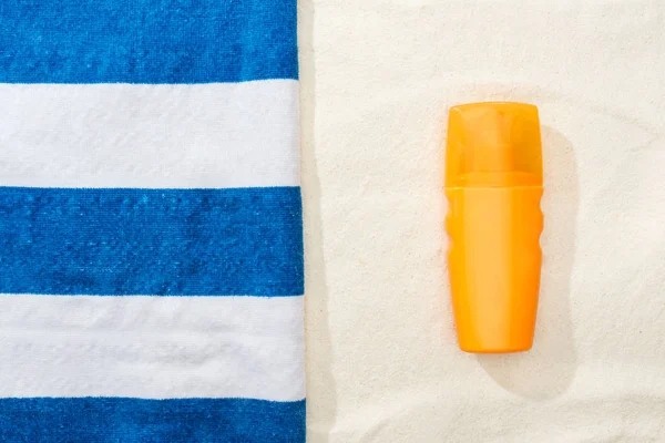 Vista superior do protetor solar e toalha azul e branca listrada na areia dourada — Fotografia de Stock