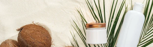 Top view of cosmetics with coconuts and palm leaves on golden sand, panoramic shot — Stock Photo