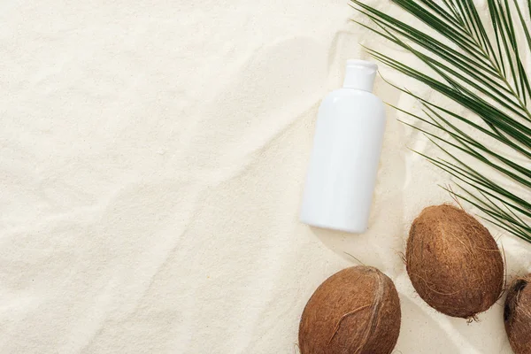 Vue du dessus de la feuille de palme, des noix de coco et du produit de protection solaire sur sable — Photo de stock