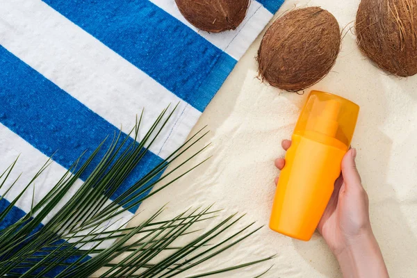 Vue du dessus de la feuille de palmier, des noix de coco et de la main féminine avec écran solaire sur sable — Photo de stock