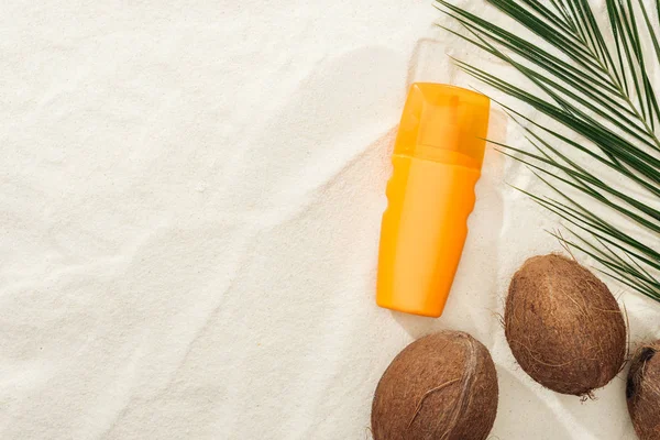 Vue du dessus de la feuille de palmier, noix de coco et crème solaire orange sur sable — Photo de stock