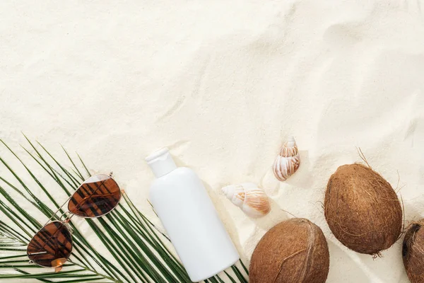 Vue de dessus des coquillages, des noix de coco et de la lotion solaire, des lunettes de soleil et des feuilles de palmier sur le sable — Photo de stock