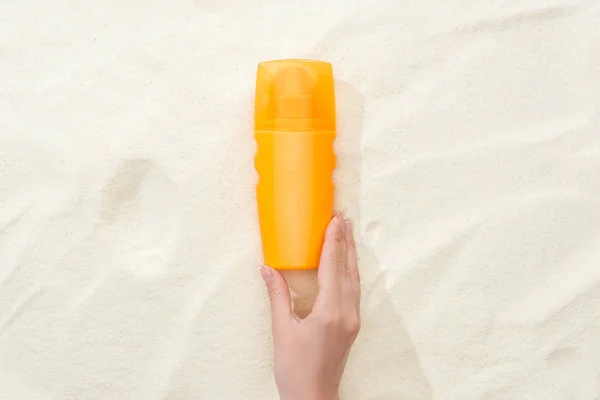 Cropped view of woman holding orange sunscreen lotion above golden sand — Stock Photo