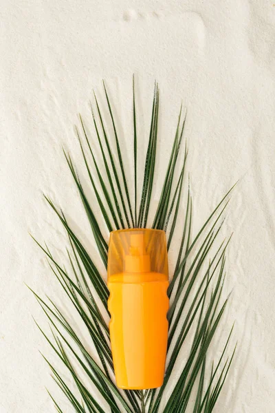 Vista superior da folha de palma e protetor solar laranja na areia — Fotografia de Stock
