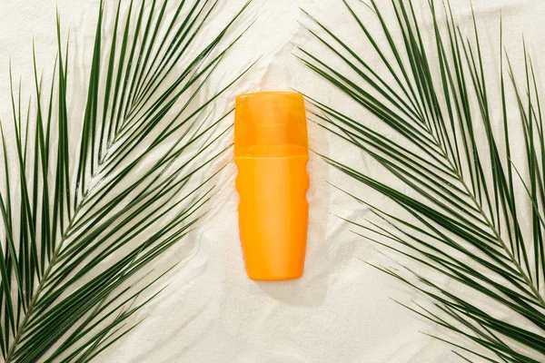 Верхний вид пальмовых листьев и оранжевый солнцезащитный крем на песке — стоковое фото