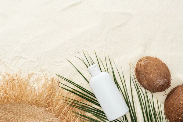 Vista superior de la hoja de palma, cocos y crema solar con sombrero de paja en la arena - foto de stock