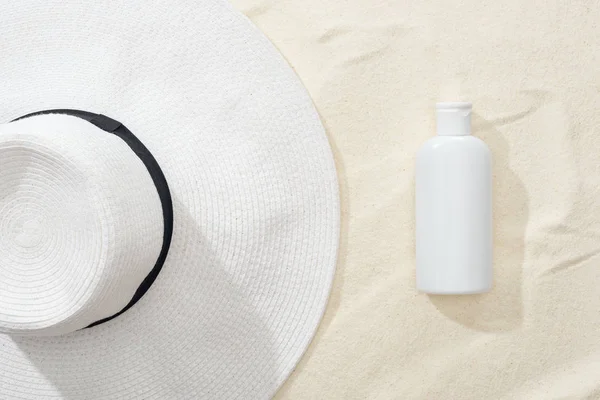 Top view of white sunscreen lotion and straw hat on sand — Stock Photo