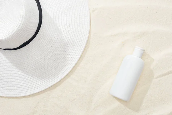 Vista superior de protector solar blanco y sombrero de paja en la arena - foto de stock