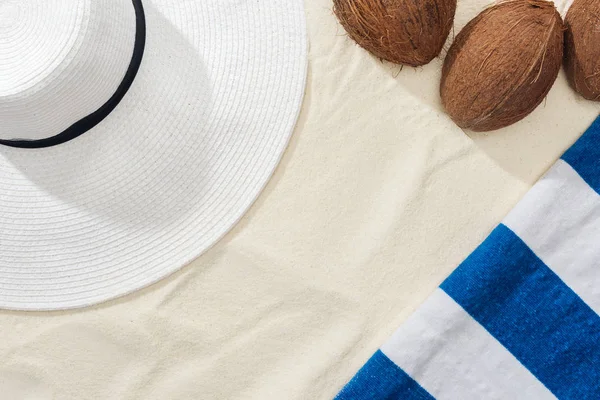 Vue du dessus des noix de coco, serviette rayée et chapeau de paille blanche sur sable — Photo de stock