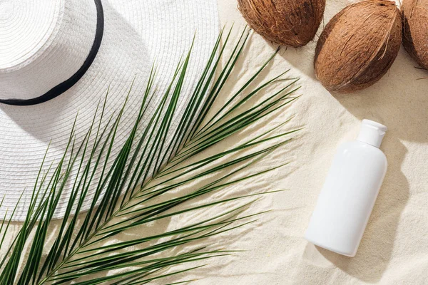 Vista dall'alto di foglie di palma, crema solare, noci di cocco e cappello di paglia bianca sulla sabbia — Foto stock