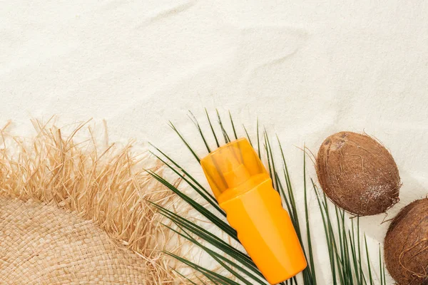 Vista superior de la hoja de palma, protector solar naranja, cocos y sombrero de paja en la arena - foto de stock