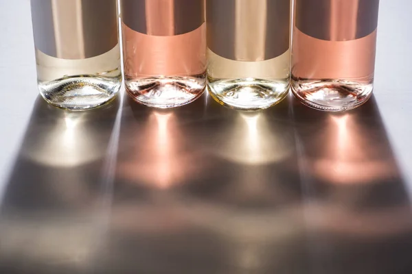 Vista de perto de garrafas de vinho branco e rosa com rótulos em branco no fundo cinza com luz — Fotografia de Stock